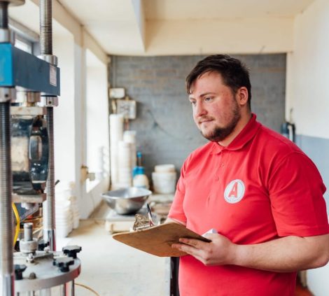 Aitken Labs technician reviewing test results beside geotechnical laboratory equipment.