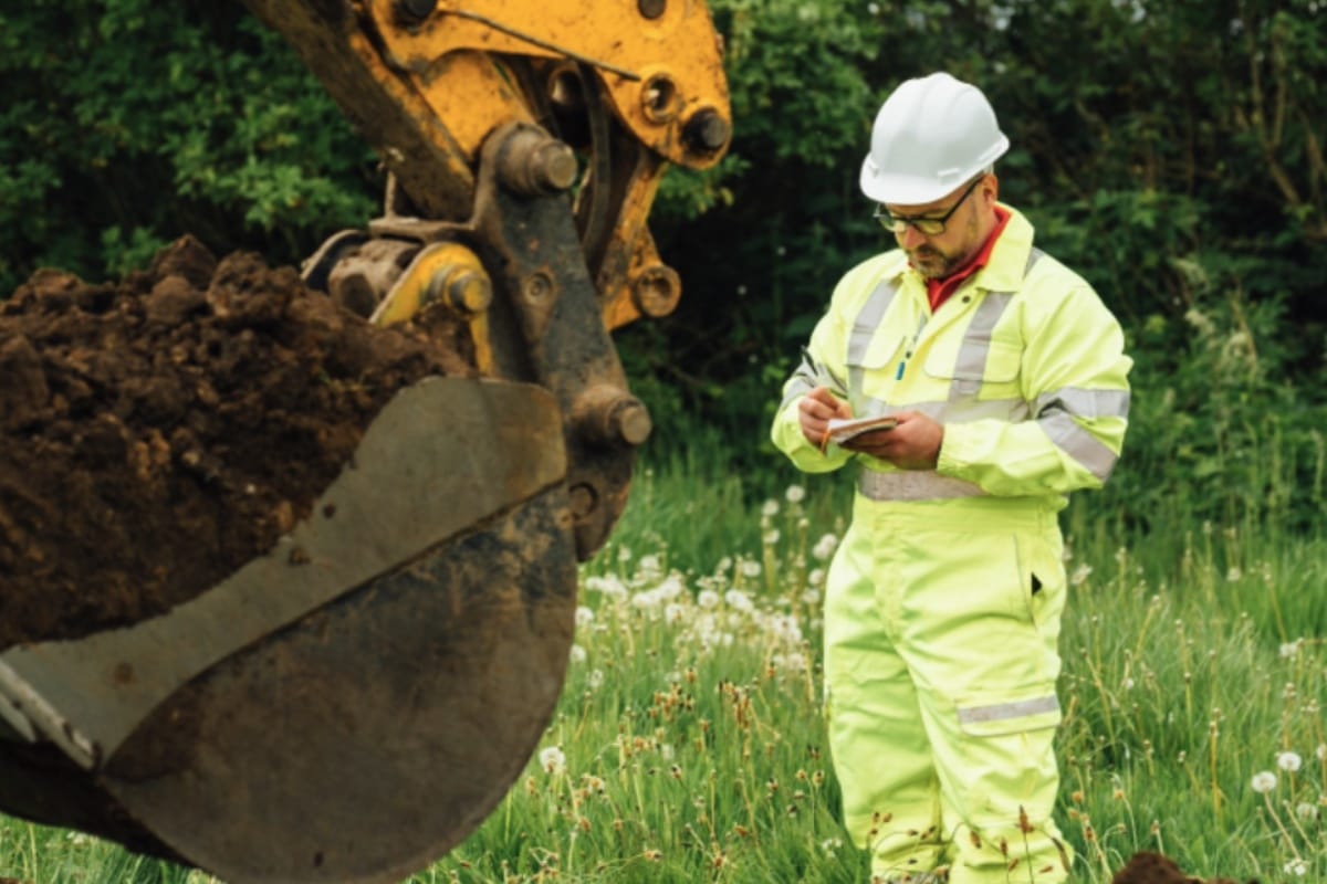 Aitken Labs engineer recording ground investigation data beside excavation machinery