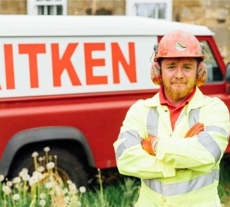 Aitken Labs field engineer standing beside branded company vehicle during site investigation work.